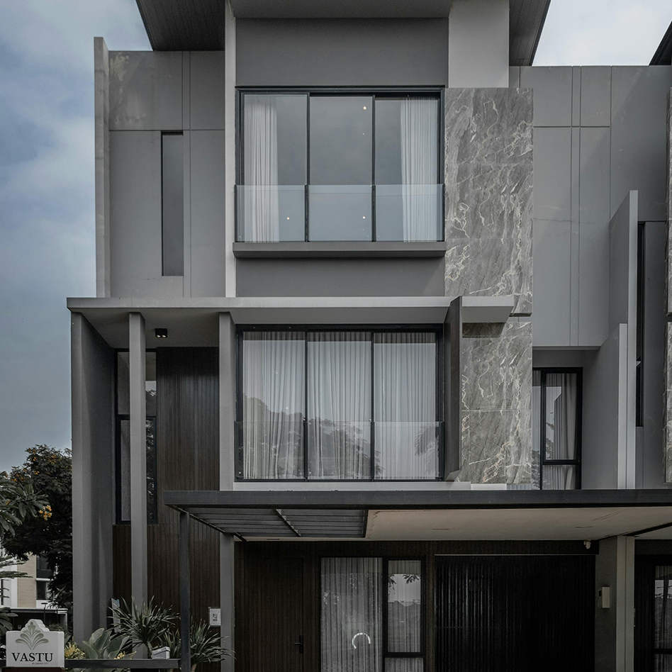 Modern three-story house with gray and stone textured exterior, large glass windows, and a covered entrance.