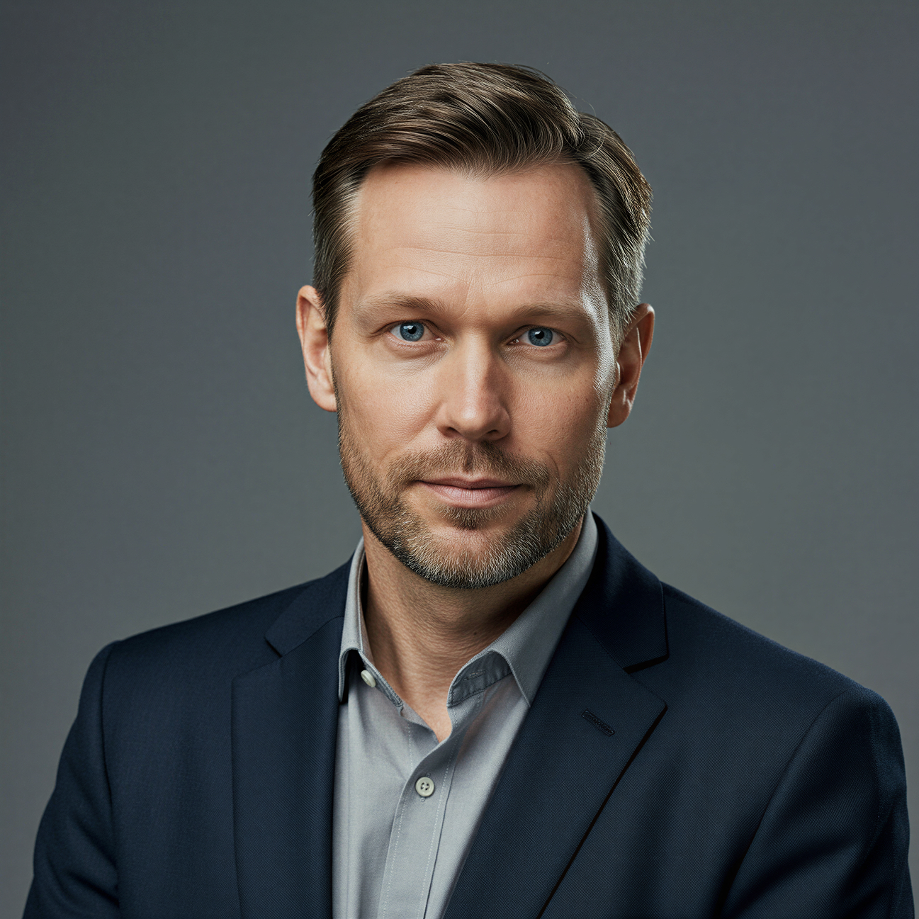 Professional portrait of a middle-aged man with blue eyes, short brown hair, and light beard wearing a navy blazer and light gray shirt.