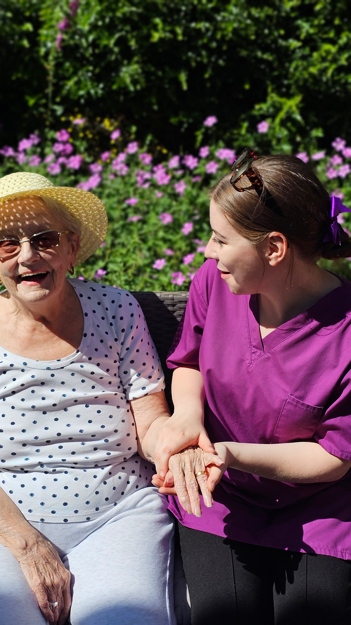 Smiling elderly man with glasses holding a smartphone in a garden with green plants in the background.