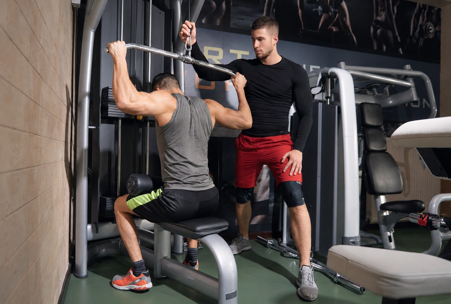 Fitness coach guiding a client through a lat pulldown exercise in a gym