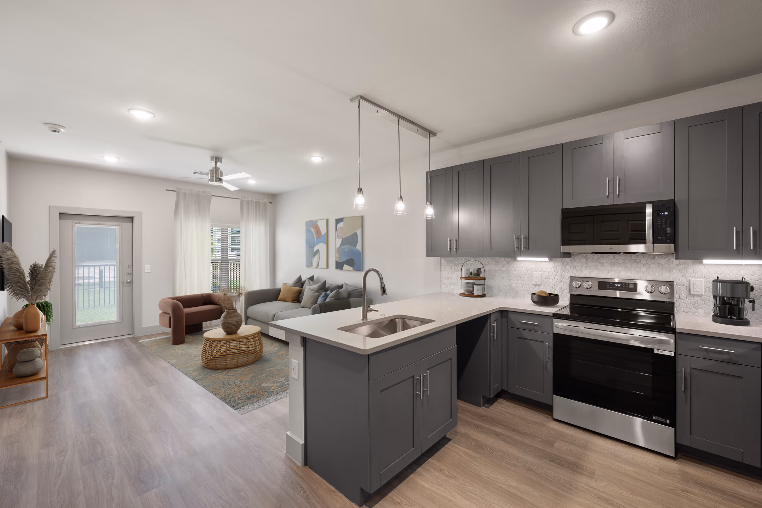 Wide view of living area with sofa, coffee table, and wall art featuring kitchen with gray cabinets and stainless steel appliances