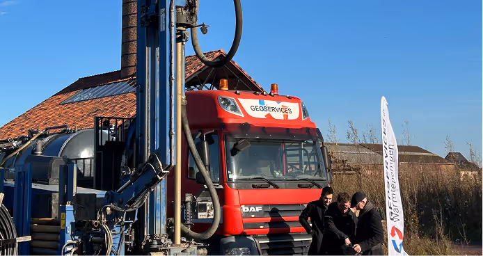 Drie mannen die op een zonnige dag apparatuur inspecteren naast een rode vrachtwagen van Geoservices en een boormachine.