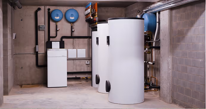 Technicus die onderhoud uitvoert aan een warmtepompsysteem met buitenunit, voorzien van witte tanks en blauwe drukvaten in een kelder.