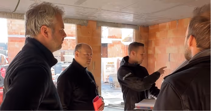 Vier mannen zijn in gesprek in een nieuwbouw met bakstenen muren.
