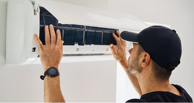 Man met pet die ventilatiesysteem van dichtbij bekijkt.