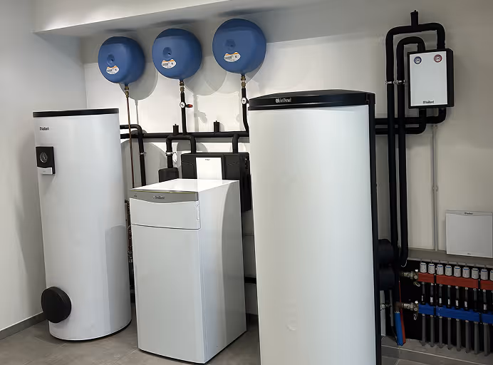 Drie witte warmtepompen met zwarte leidingen en drie blauwe tanks die aan de muur zijn bevestigd