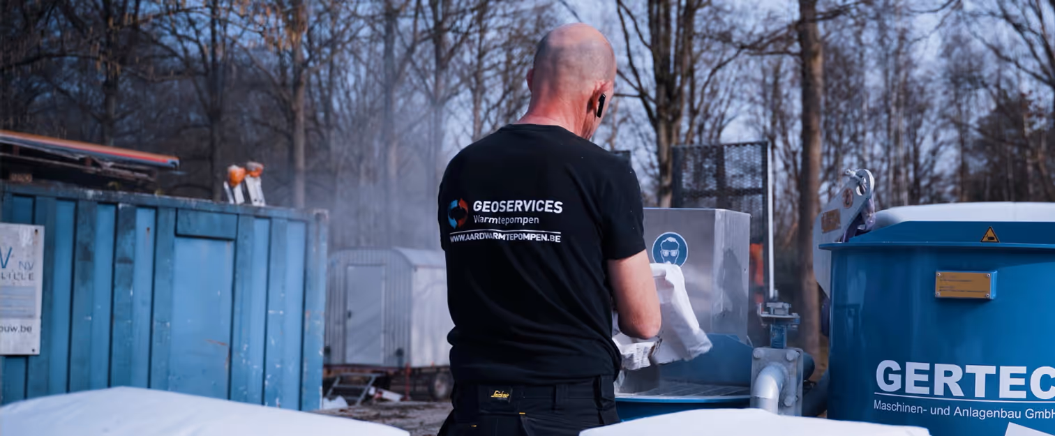 Een man in een GEOSERVICES-shirt die buiten bij industriële apparatuur aan het werk is, met kale bomen op de achtergrond.