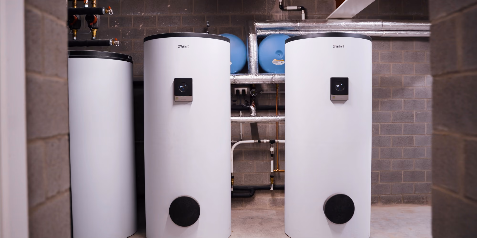 Twee grote witte Vaillant-boilers met digitale displays en buizen in een technische ruimte.