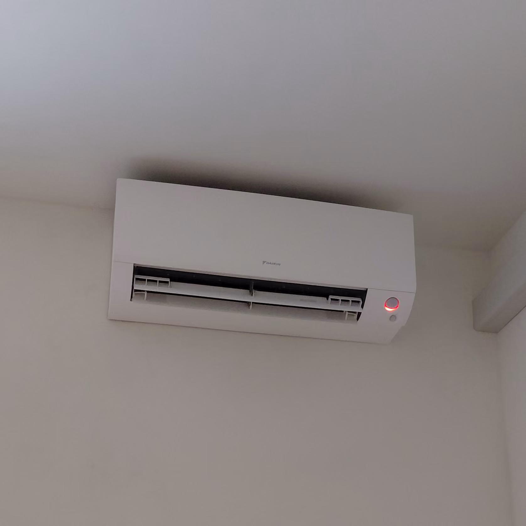 Wandgemonteerde witte airconditioner met rode indicatorlamp aan de rechterkant.