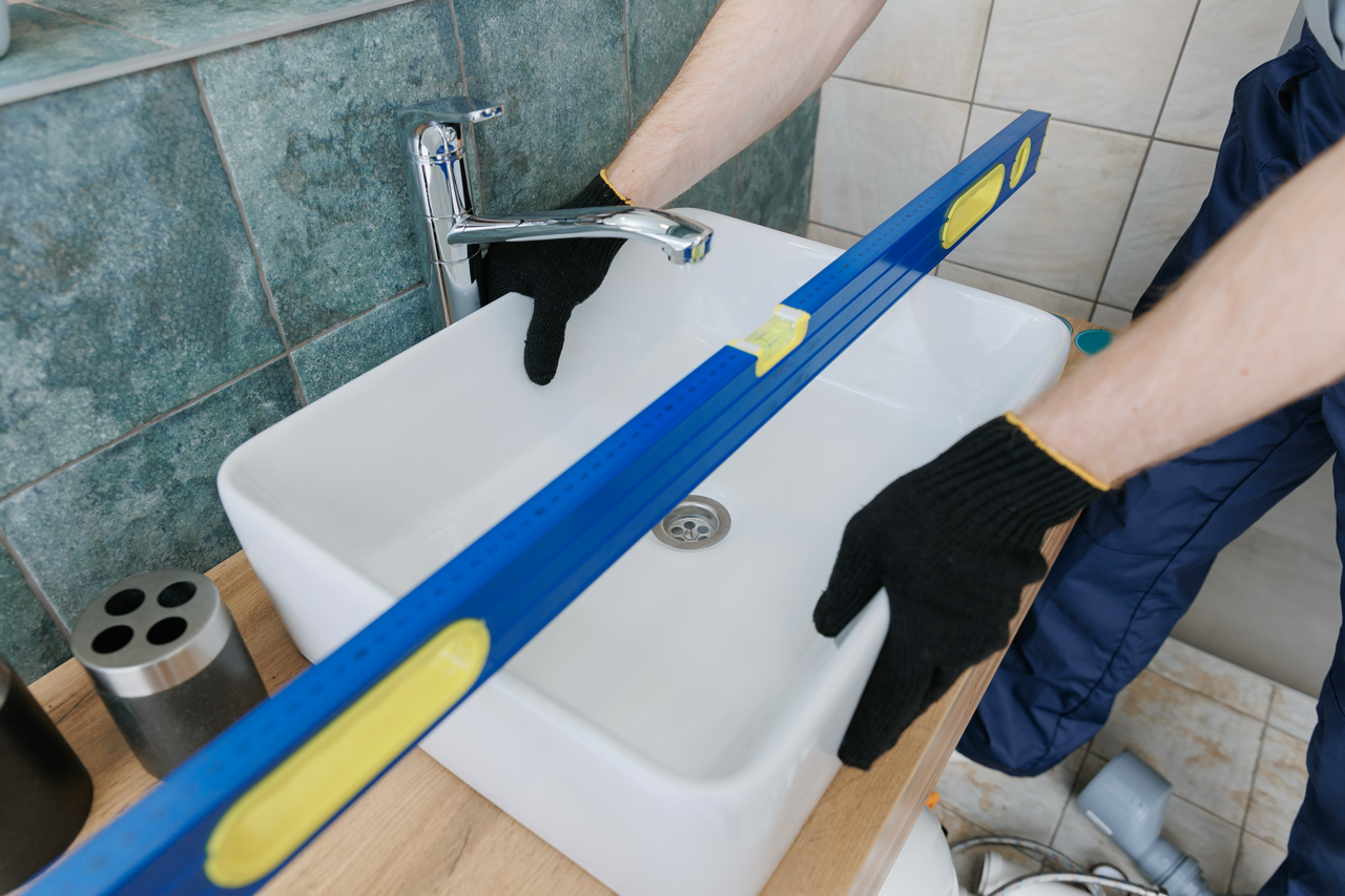 Een persoon meet het waterpas van een witte wastafel met een blauwe waterpas in een badkamer.