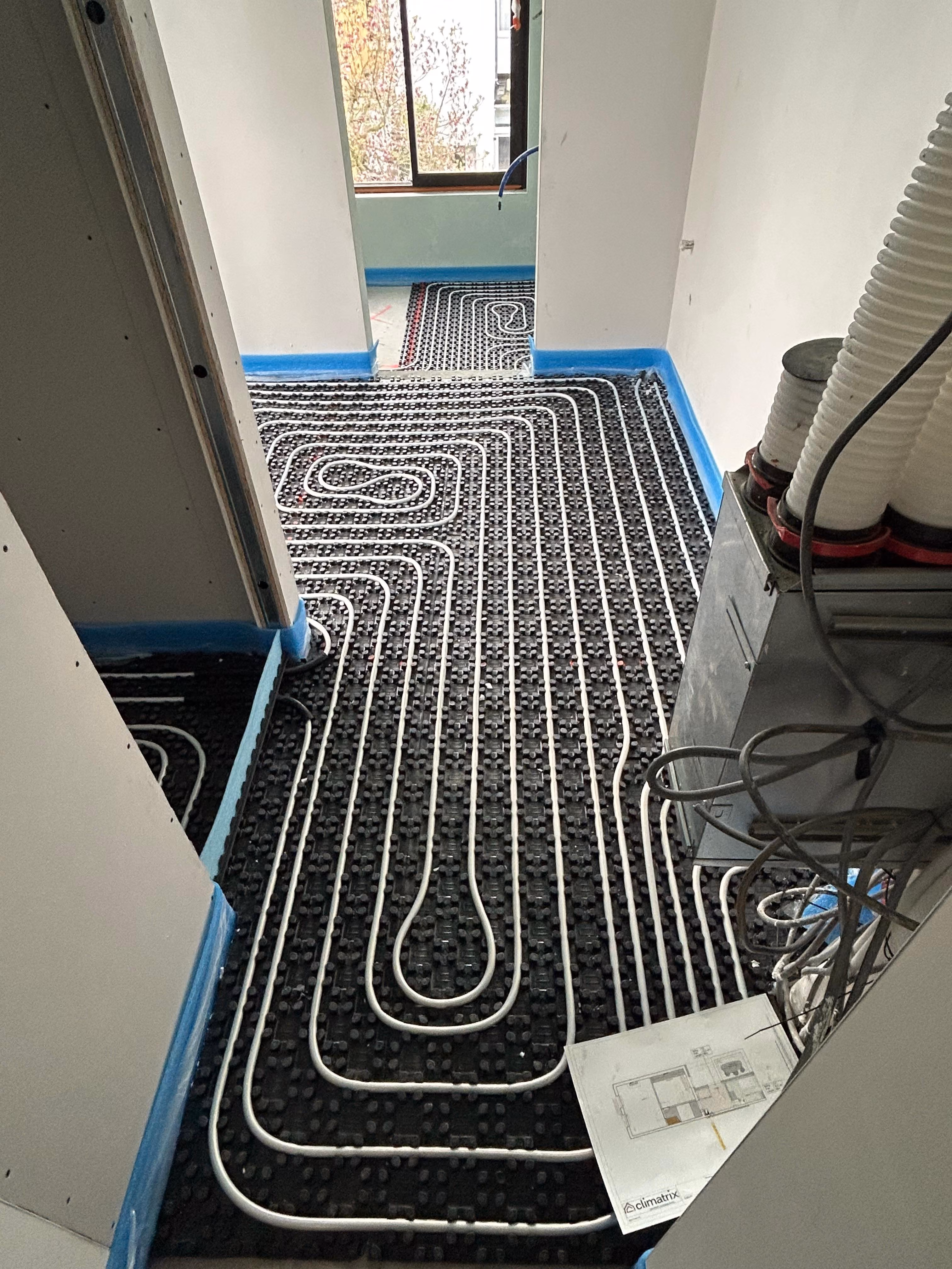 Vloerverwarming in een droog systeem met witte buizen over zwart matten.