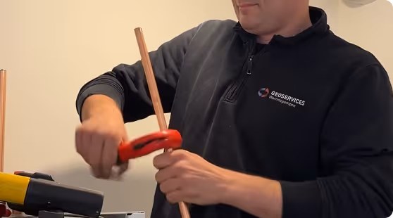 Sanitair installateur van Geoservices snijdt een koperen leiding op maat
