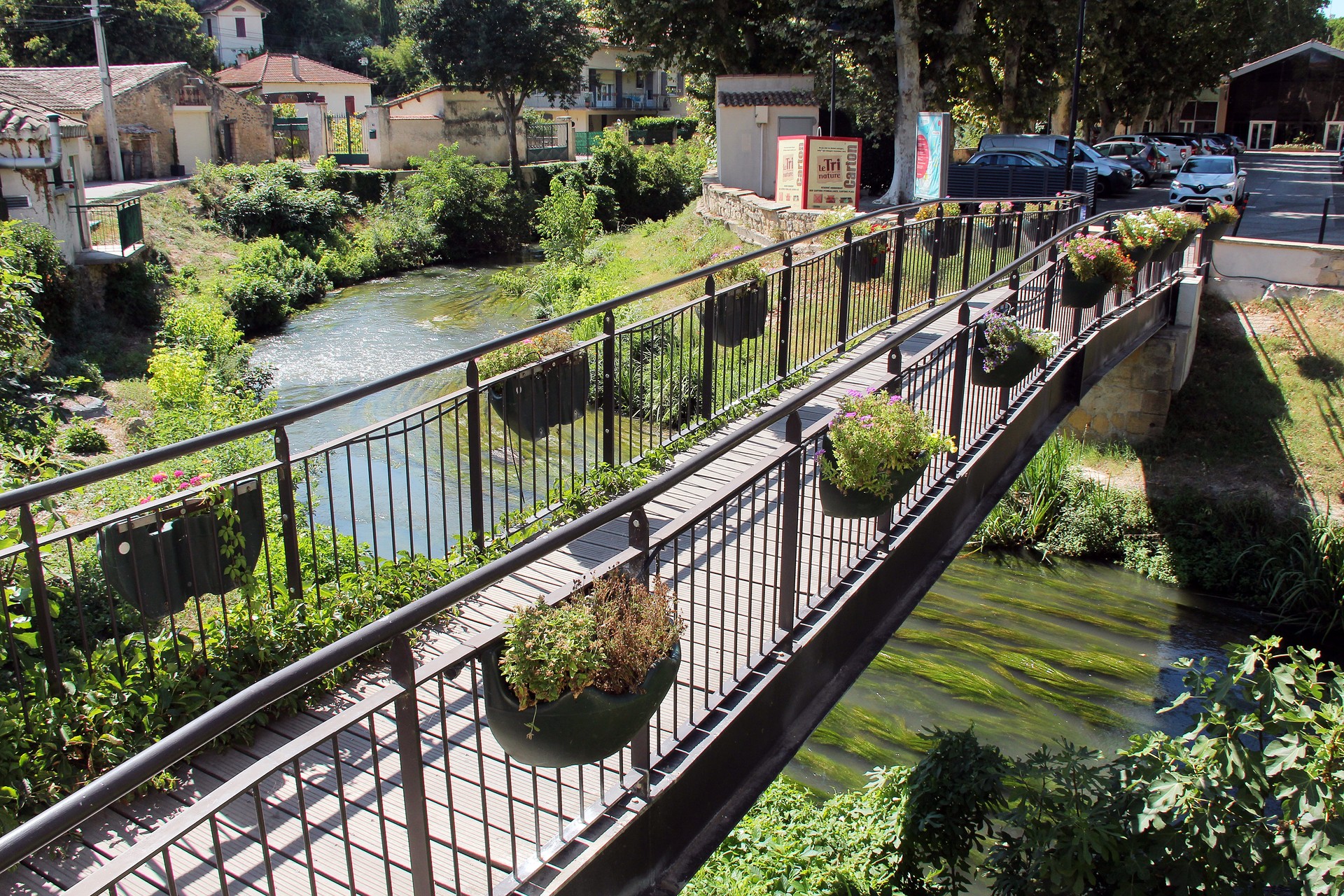 Passerelle décorée de jardinières fleuries au-dessus d'une rivière dans un village tranquille.