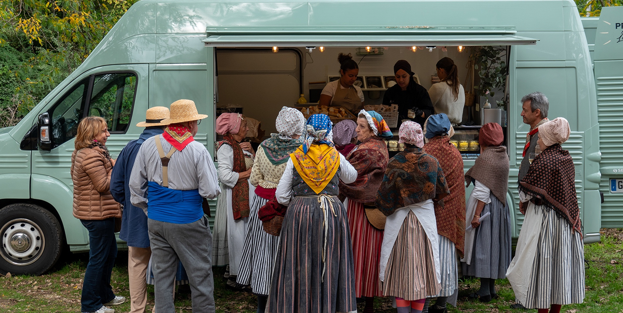 Groupe en habits traditionnels faisant la queue devant un camion alimentaire vert clair en plein air.