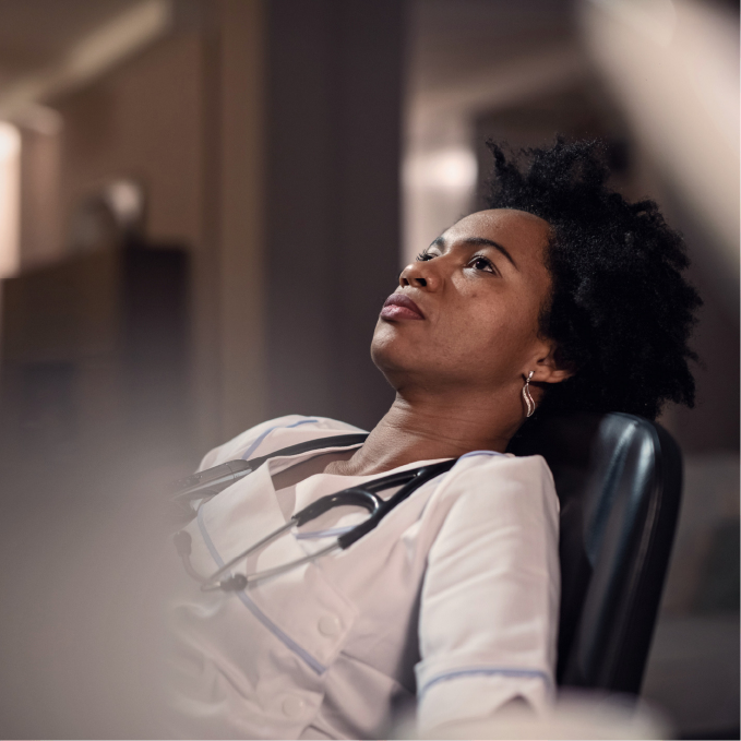 Thoughtful female doctor in white coat with stethoscope reclining and looking upward.