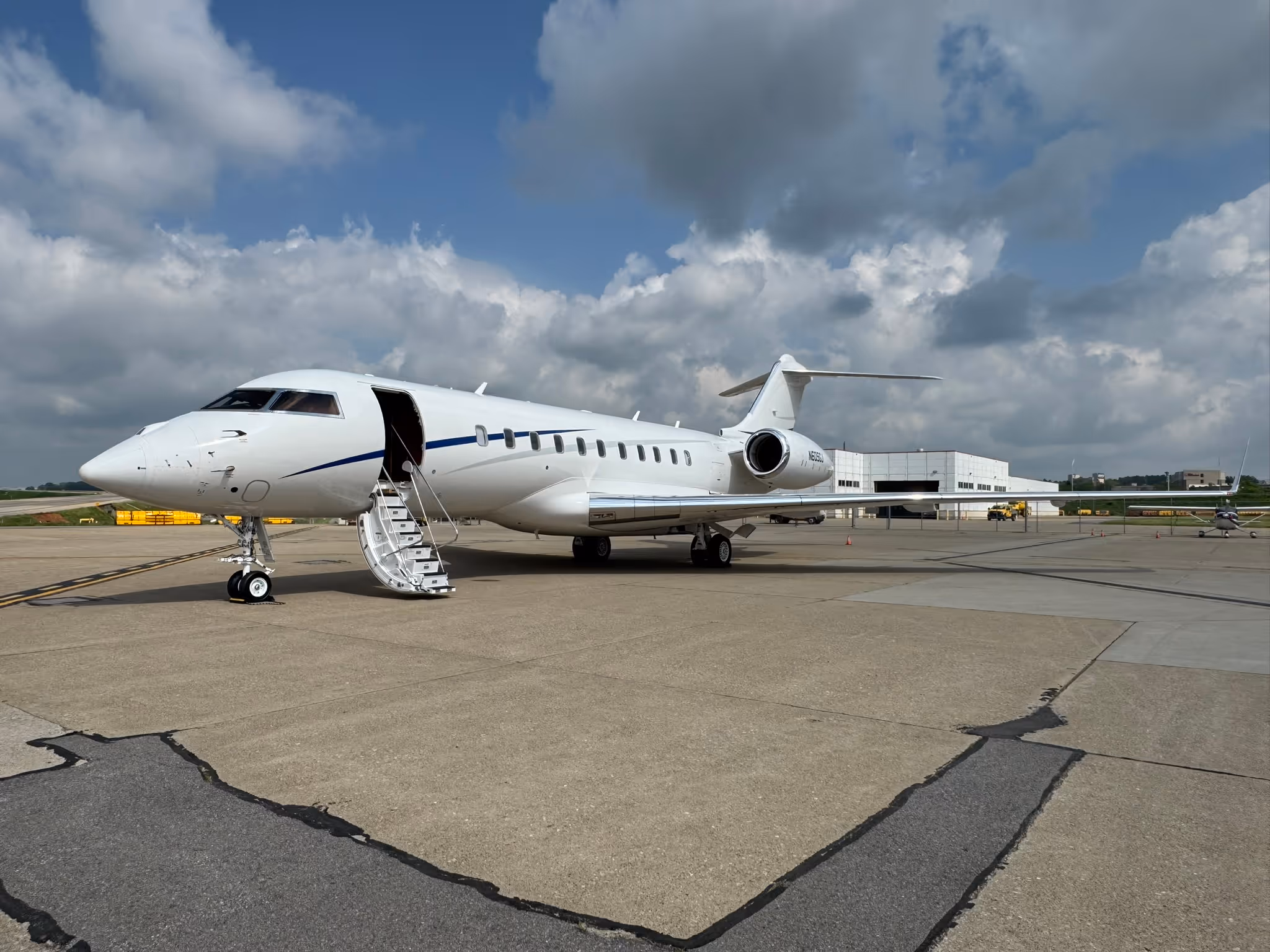 White private jet with open door and stairs parked on airport tarmac under cloudy sky.