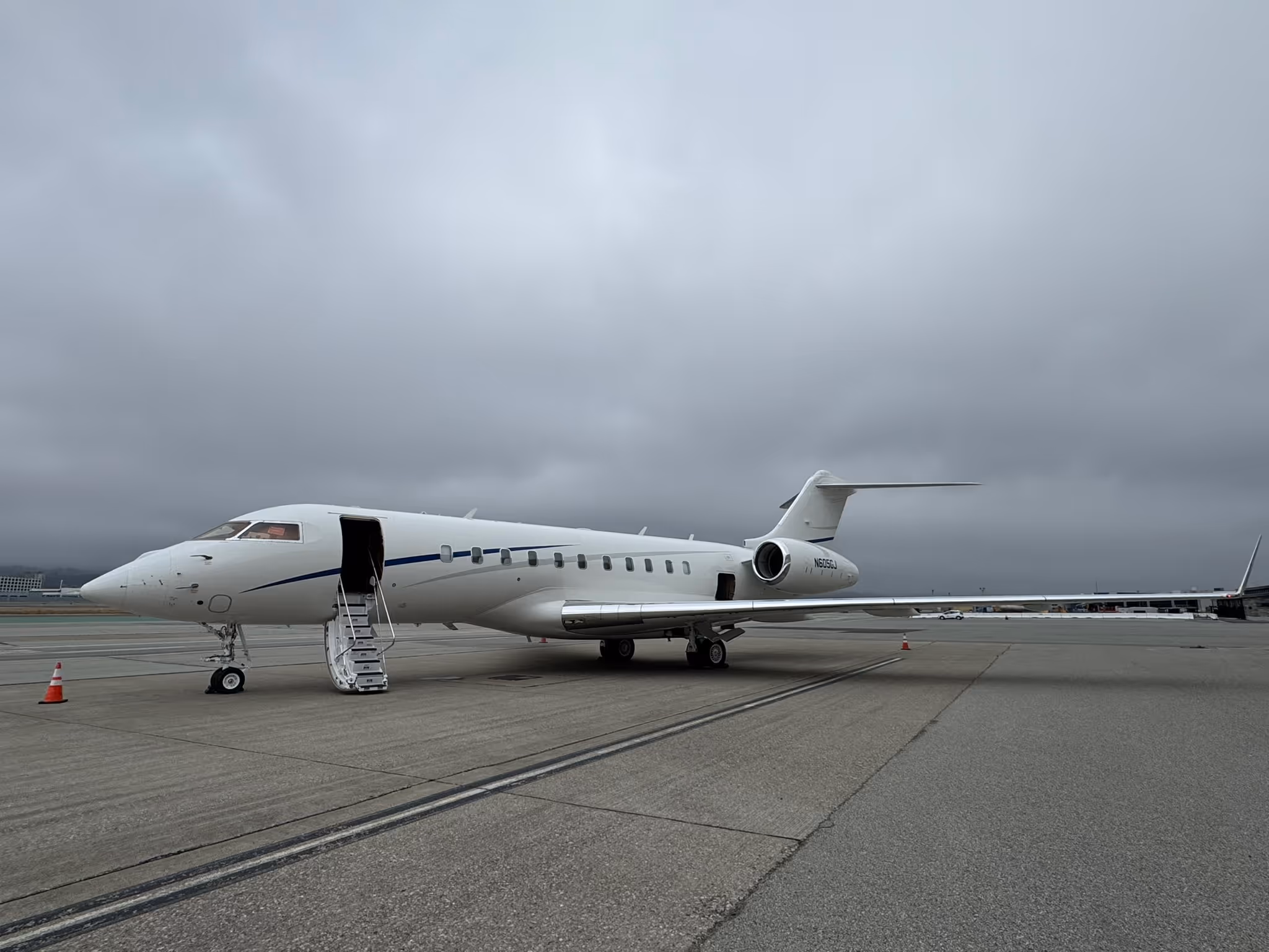 White private jet parked on tarmac under cloudy sky with open door and stairs down.
