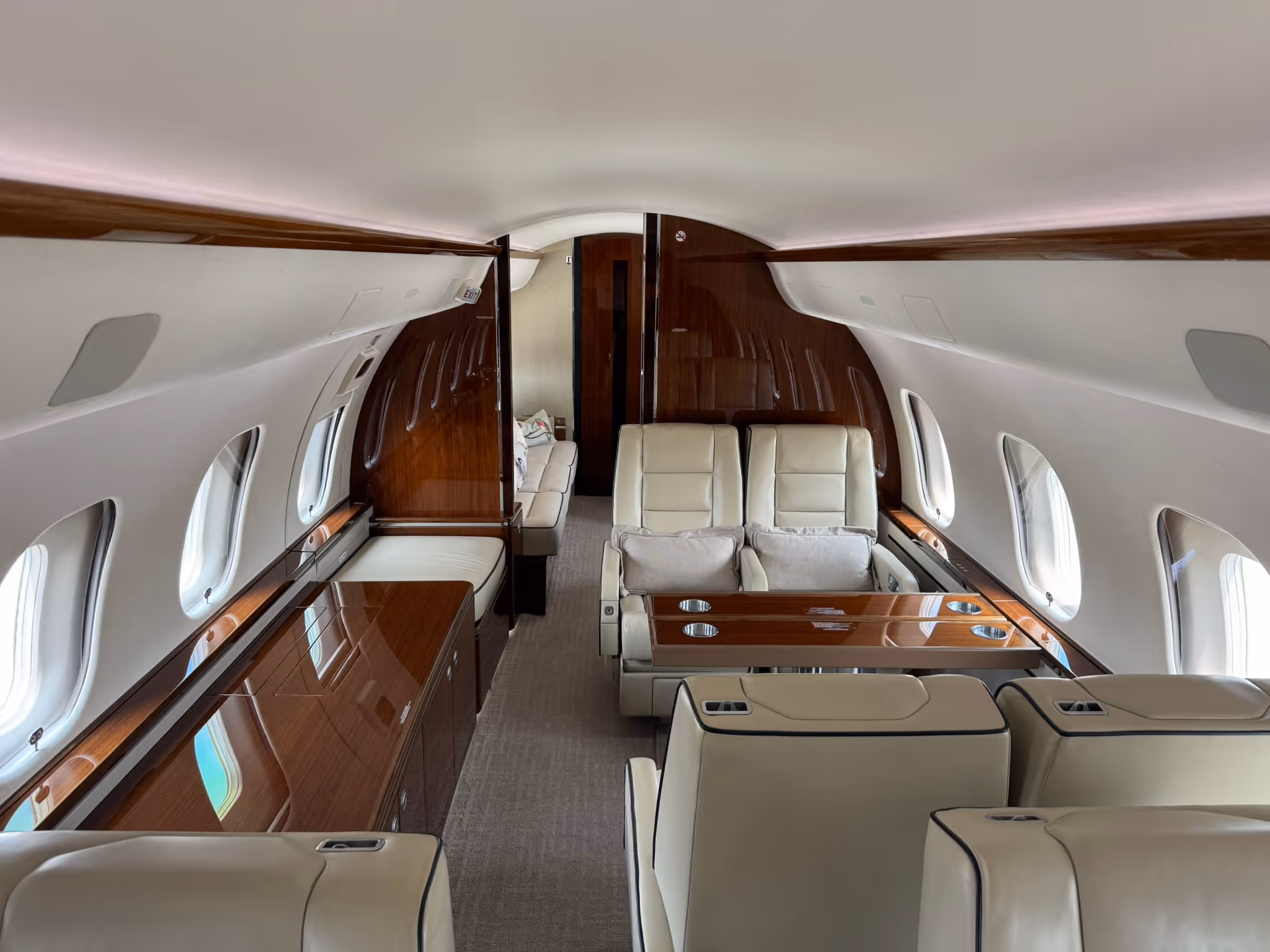 Luxurious private jet cabin with cream leather seats, wooden table, and large windows.