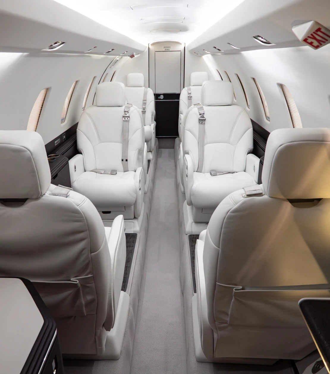 Interior of private jet with six white leather seats arranged in pairs along a central aisle.