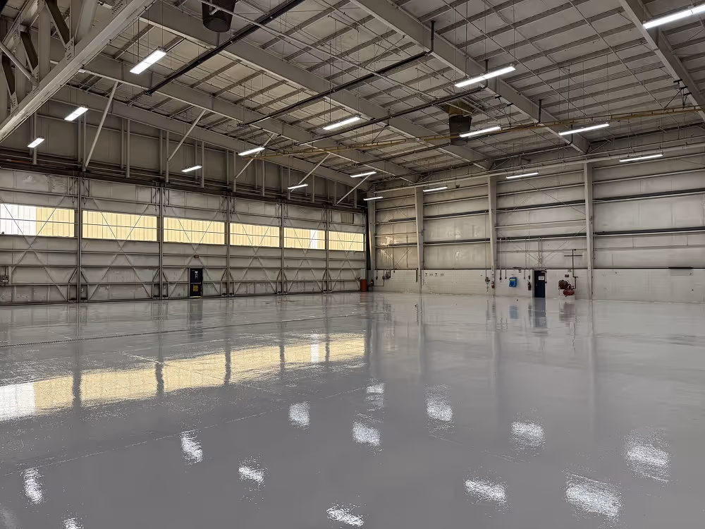 Empty large industrial warehouse with shiny, reflective floor and overhead fluorescent lights.