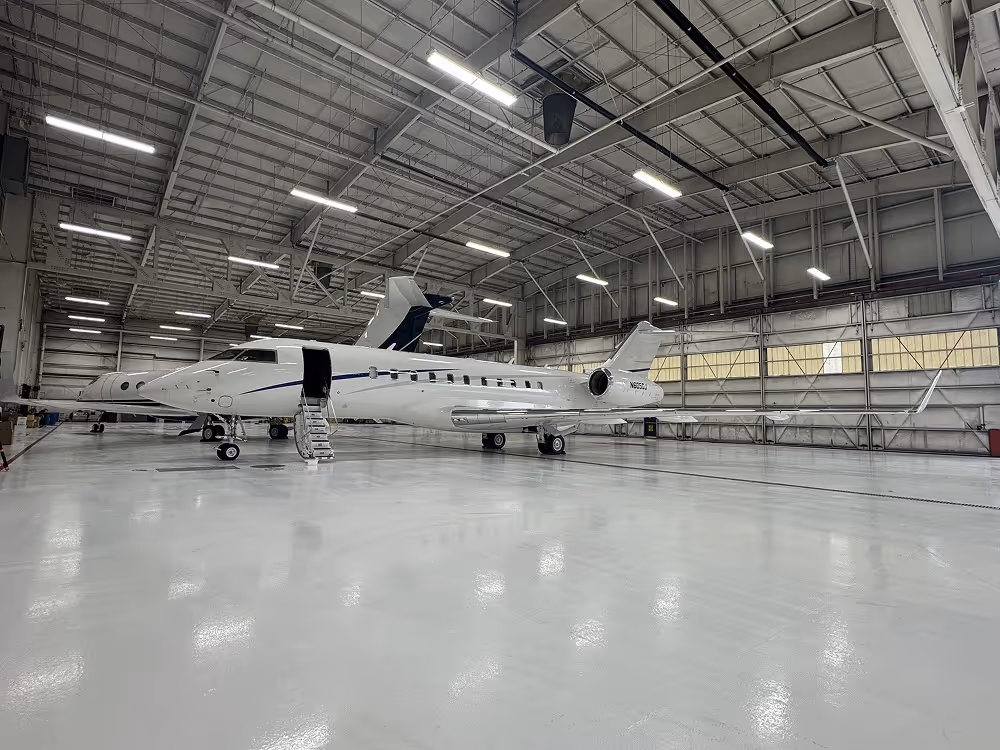 Two private jets parked inside a large, well-lit aircraft hangar with open jet stairs.