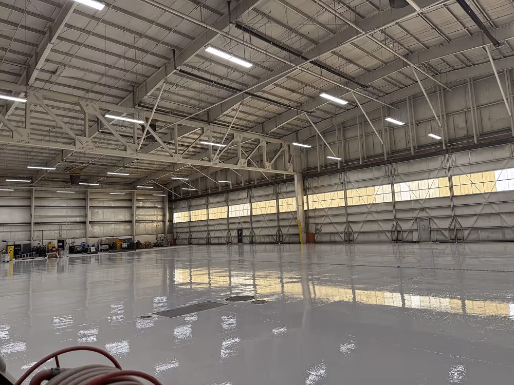 Empty large industrial hangar with shiny polished floor and overhead fluorescent lights.