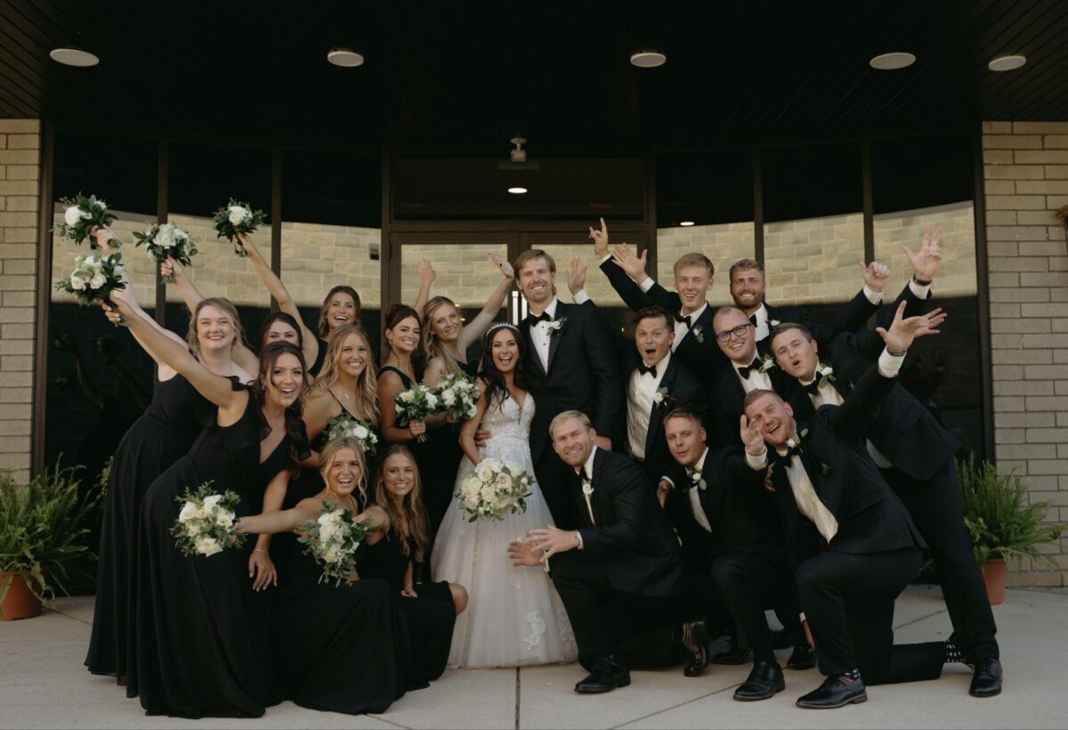 A joyful wedding party poses for a photo outside, capturing a moment of love and celebration at the enchanting Port 393.