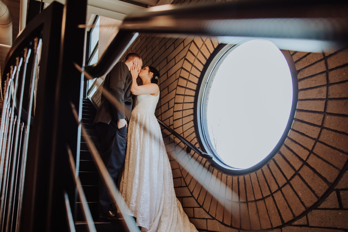 A bride and groom share a kiss on the stairs of a building.