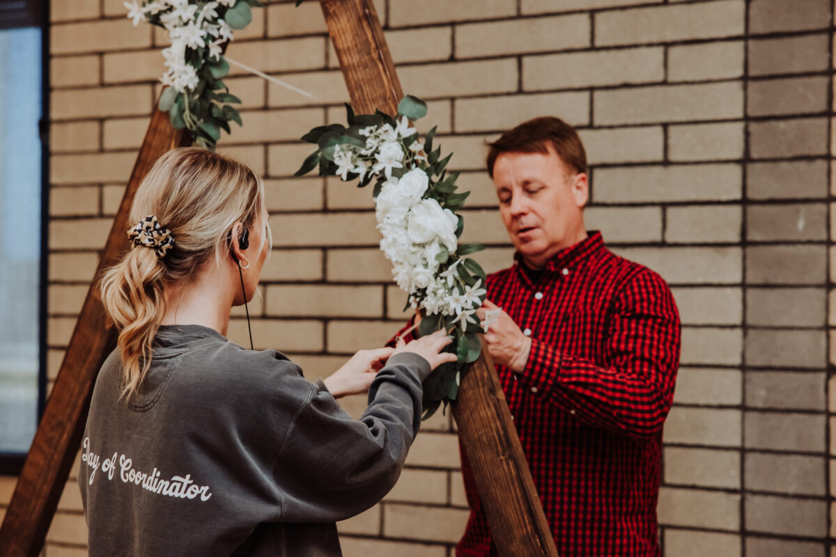 A man and woman arranging flowers on a wooden frame at Nicole & Austin’s wedding