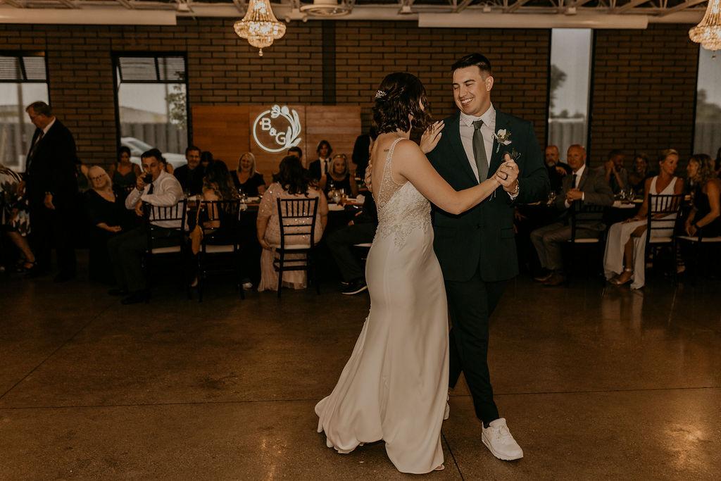 Couple dancing romantically at a warehouse wedding, surrounded by string lights and rustic decor.