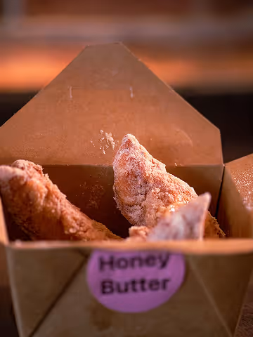 Close-up of crispy fried chicken wings in a brown takeout box labeled Honey Butter.