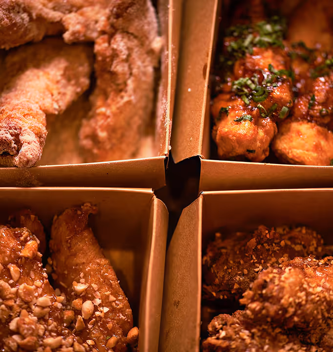 Four cardboard boxes each containing a different style of fried chicken wings with various seasonings and toppings.