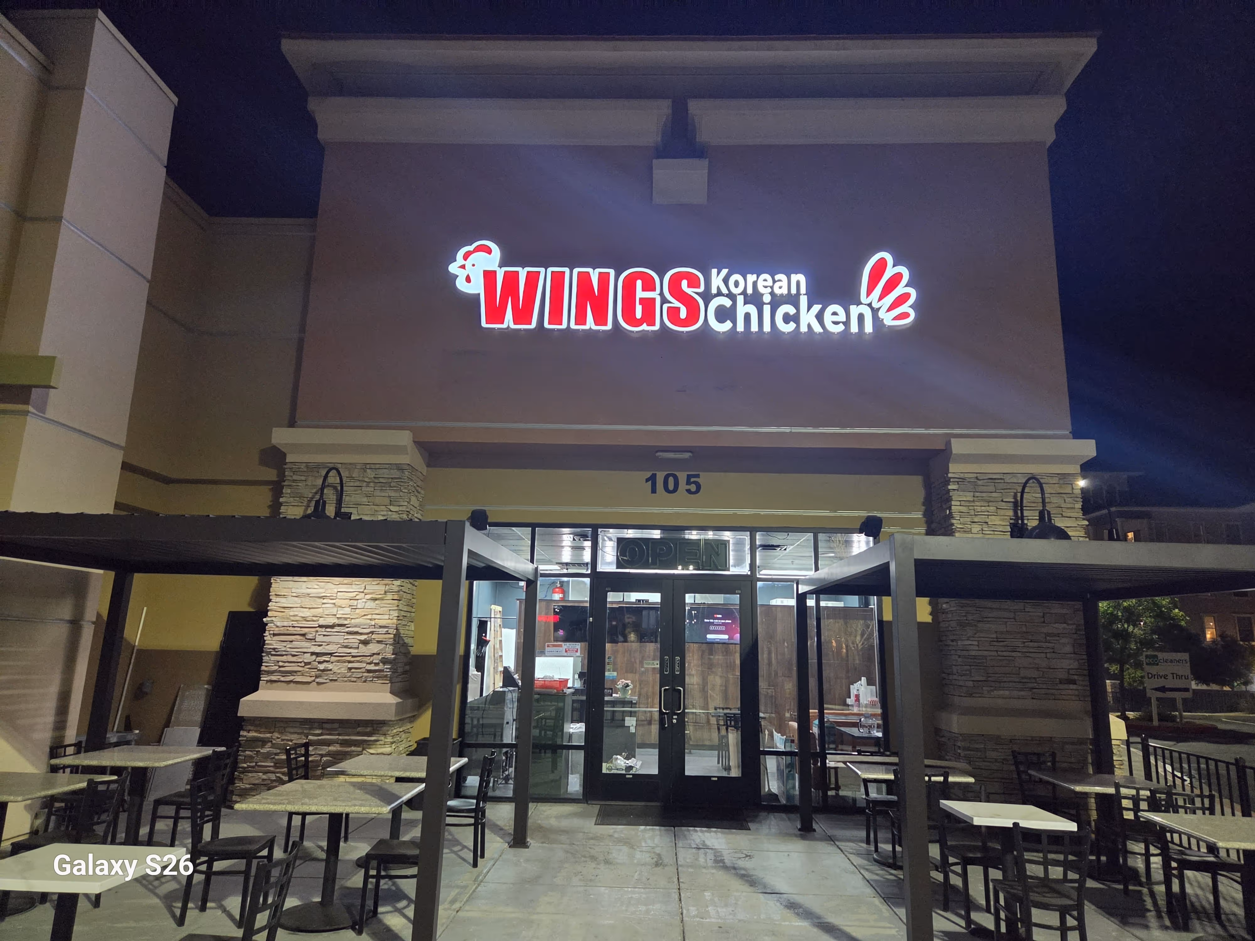 Storefront of a strip mall with signs for 'Wings Korean Chicken' and 'Macho Tequila's' under a partly cloudy sky.