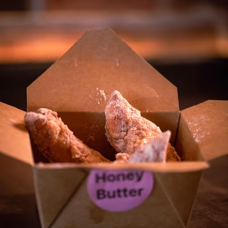 Three pieces of crispy fried chicken in an open brown takeout box labeled Honey Butter.