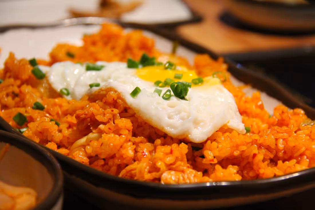 Kimchi fried rice topped with a fried egg and chopped green onions on a black-edged white plate.