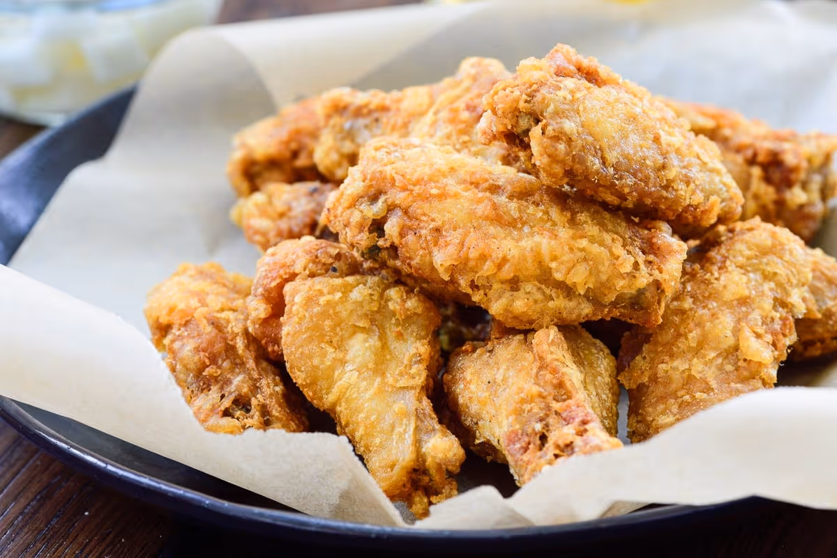 Plate of crispy golden fried chicken wings on parchment paper.