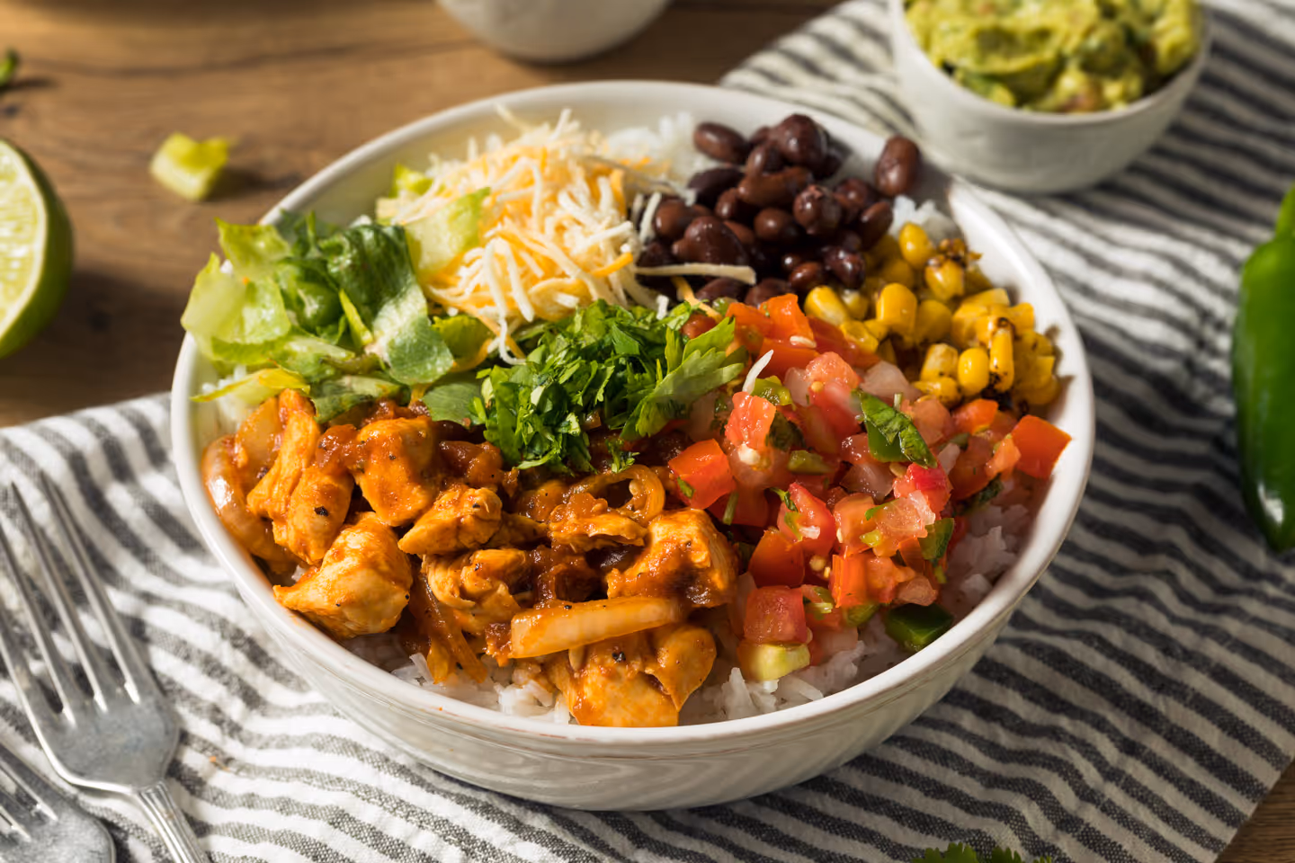 Burrito bowl with grilled chicken, black beans, corn, diced tomatoes, shredded cheese, lettuce, and cilantro over white rice.