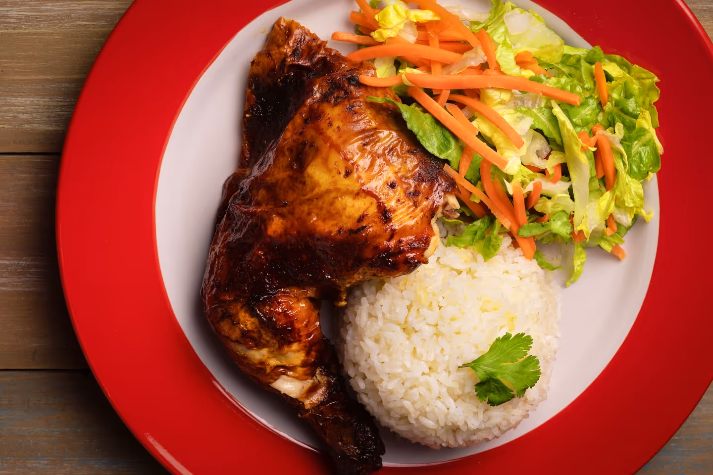 Plate with grilled chicken thigh, white rice garnished with cilantro, and a salad of lettuce and shredded carrots.