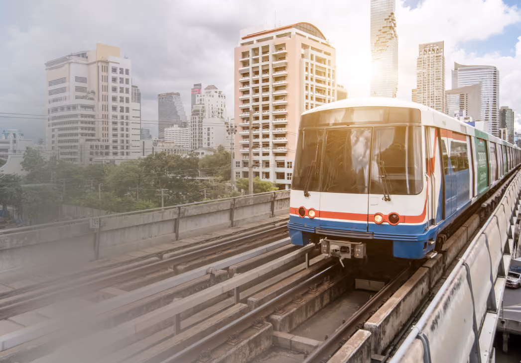 Modern train on elevated tracks with city skyscrapers in background under partly cloudy sky.