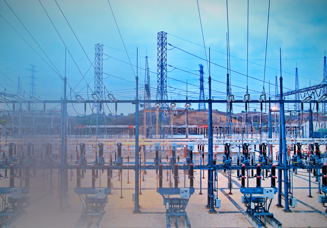 Electrical power substation with numerous transformers and transmission lines under a clear blue sky.