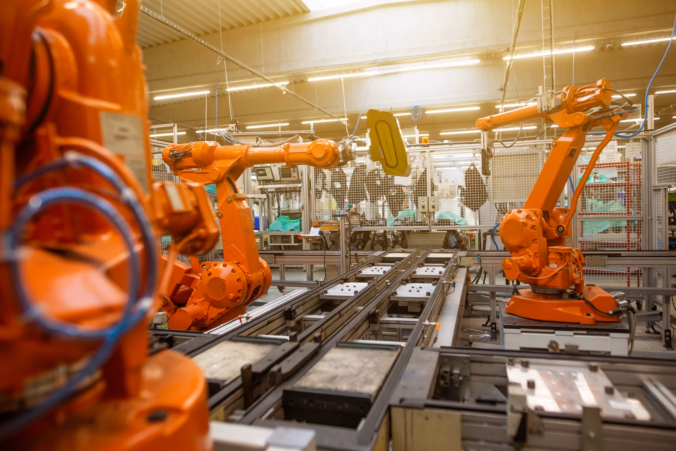 Orange industrial robotic arms operating on a factory assembly line with metal frameworks and equipment.