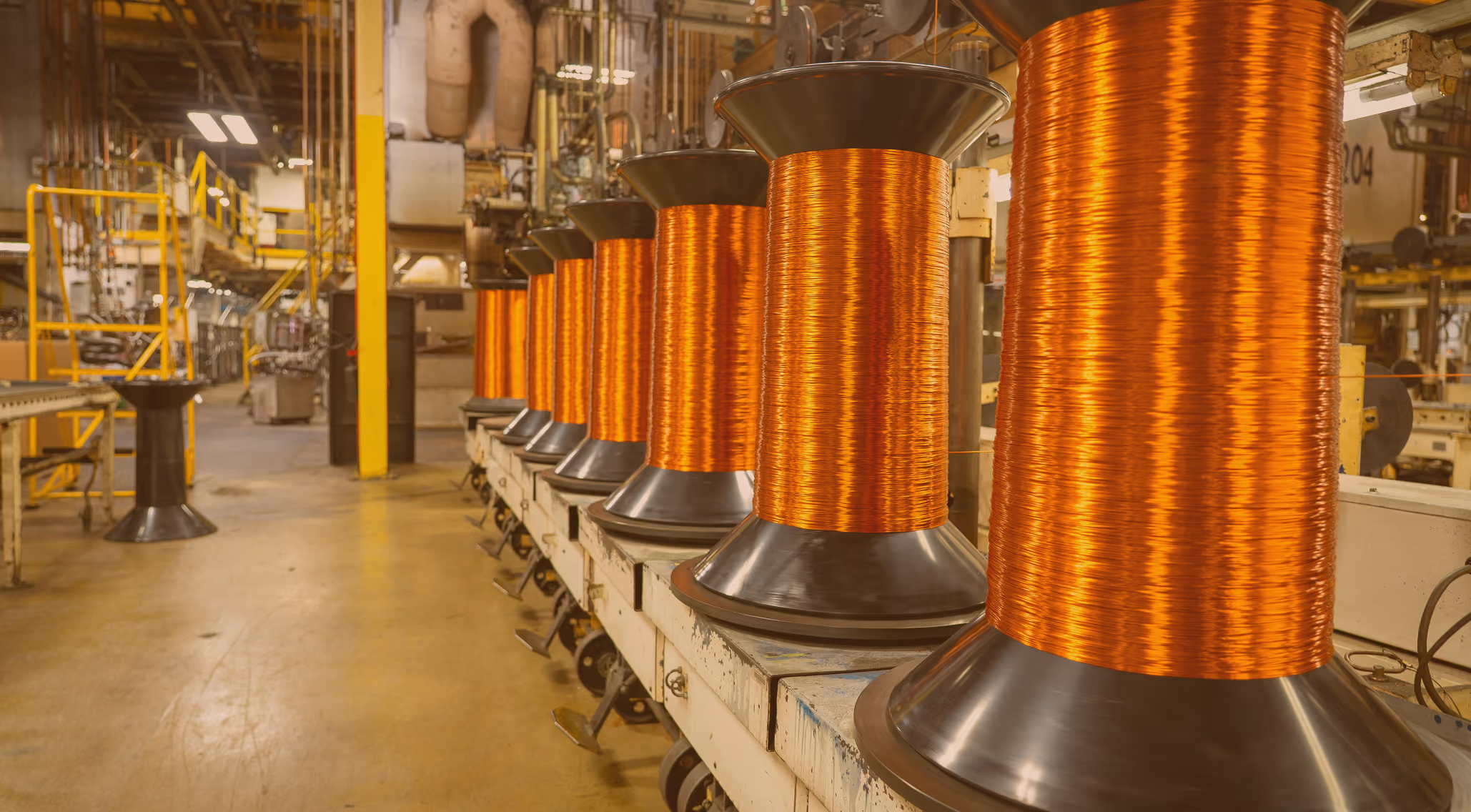 Large spools of orange copper wire lined up in an industrial factory setting.