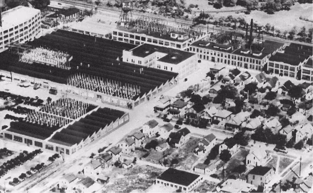 Aerial black and white photo of an industrial factory complex next to a residential neighborhood.