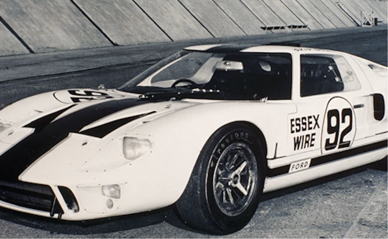 Vintage white Ford race car with black stripe and number 92 parked on a race track.