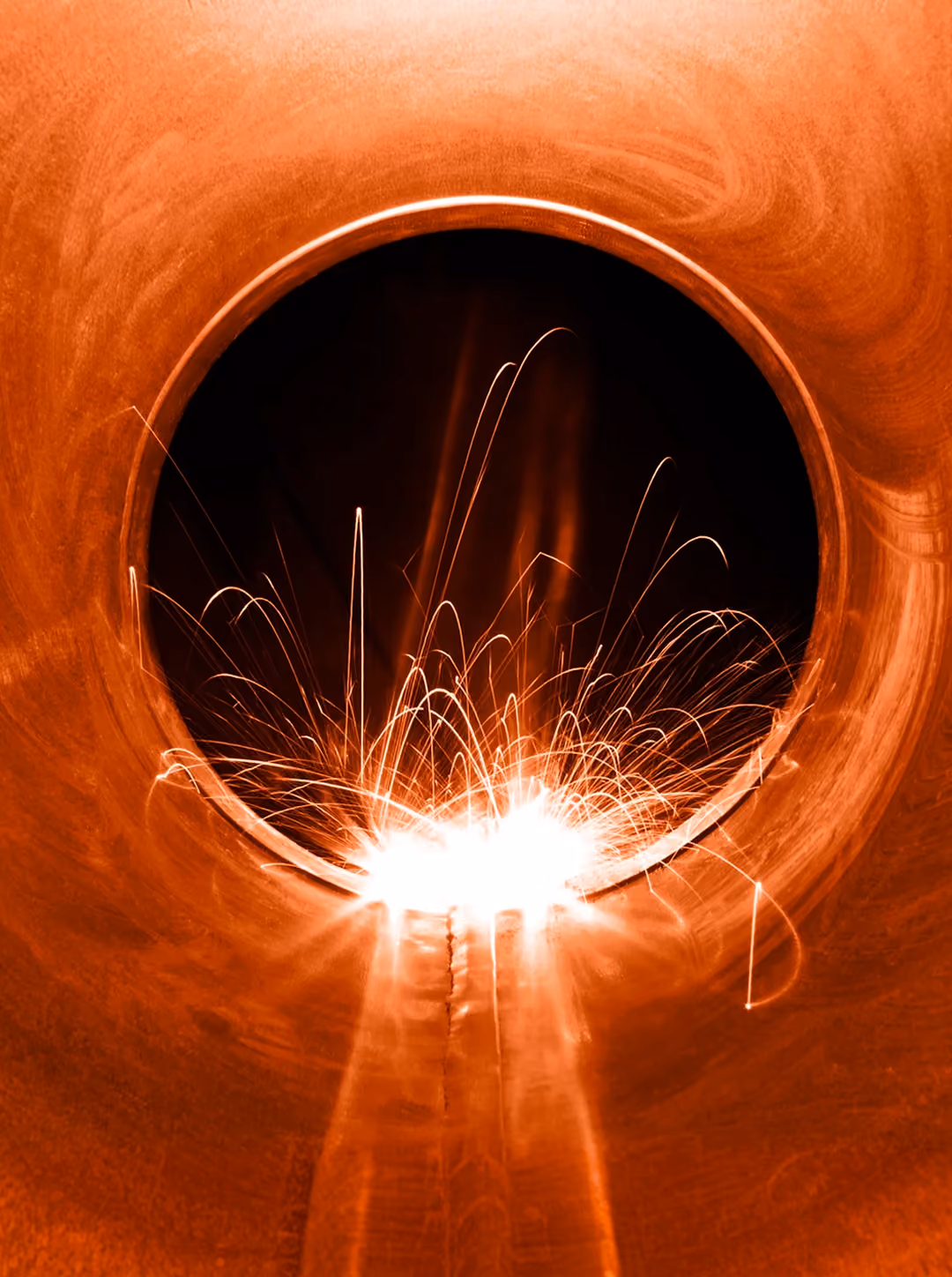 Bright sparks flying inside a large rust-colored metal pipe during welding work.