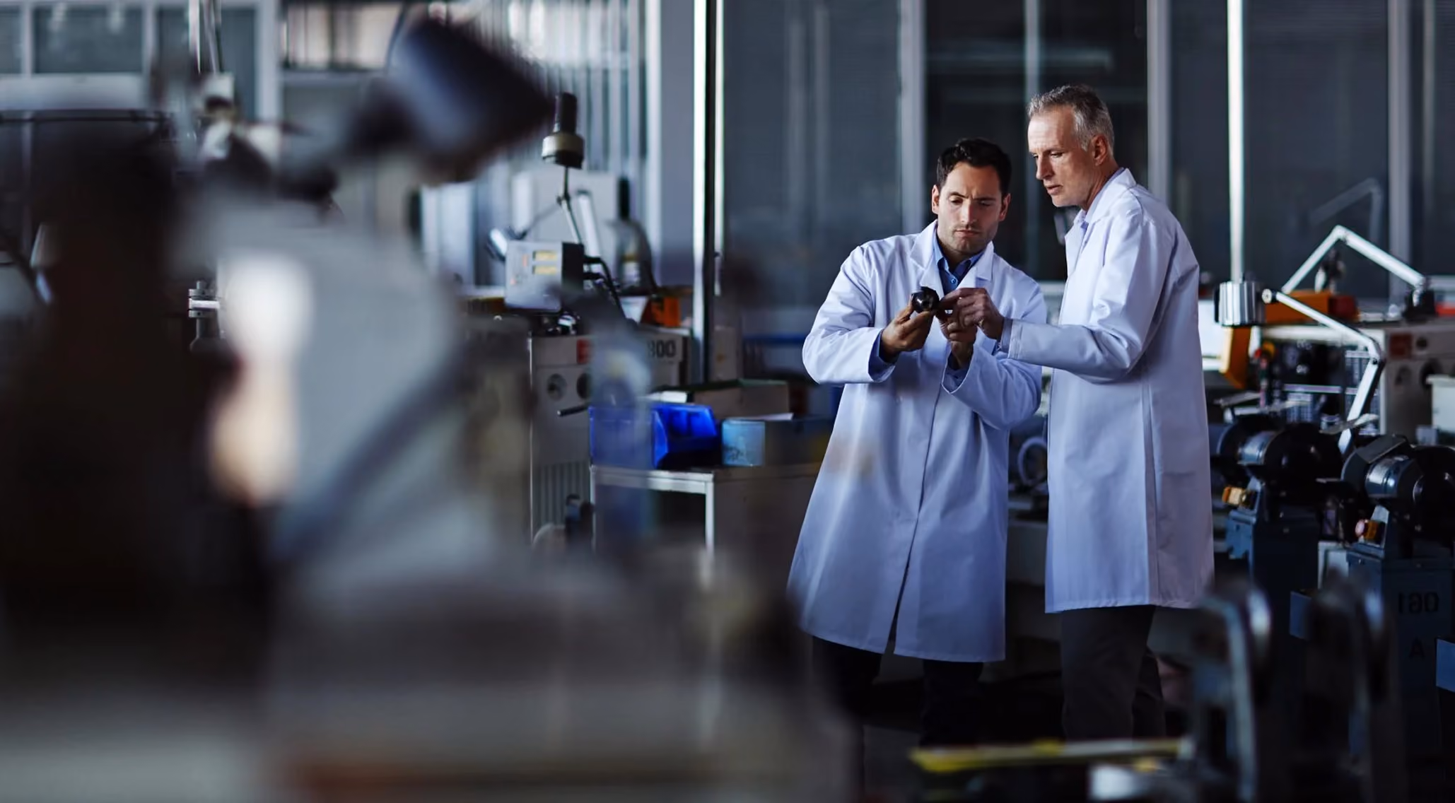 Two scientists in white lab coats examining a small device in a laboratory setting.