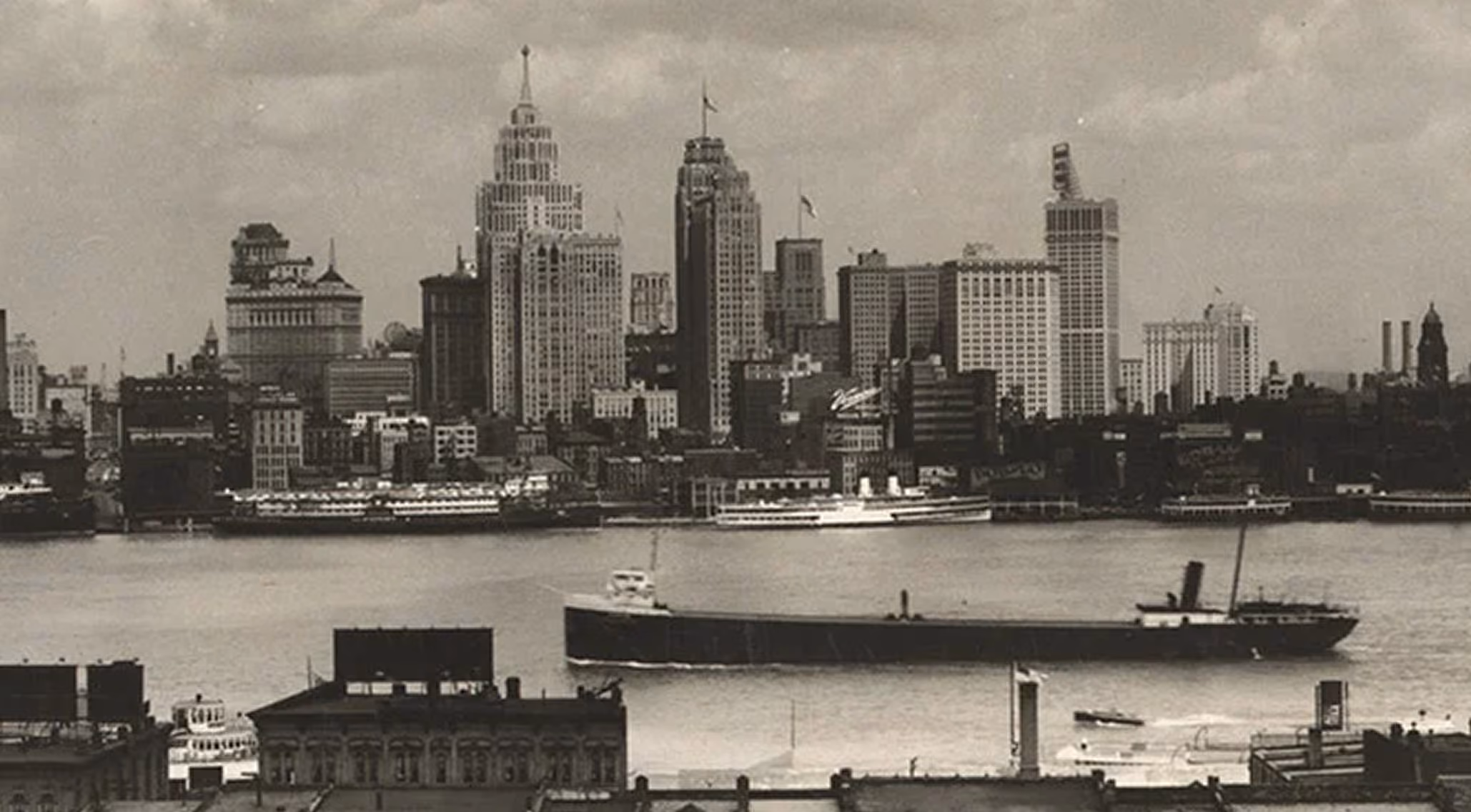 Black and white photo of an early 20th-century city skyline with a large ship on a river.