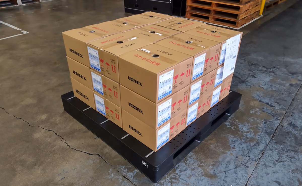 Stack of labeled cardboard boxes on a black plastic pallet inside a warehouse.