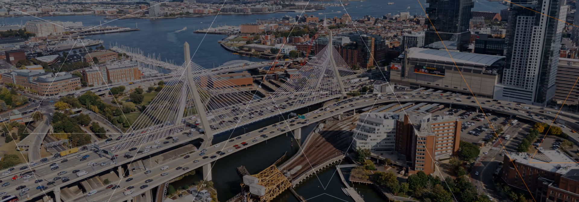 Aerial view of a cable-stayed bridge with traffic over a river in a cityscape with buildings and boats.