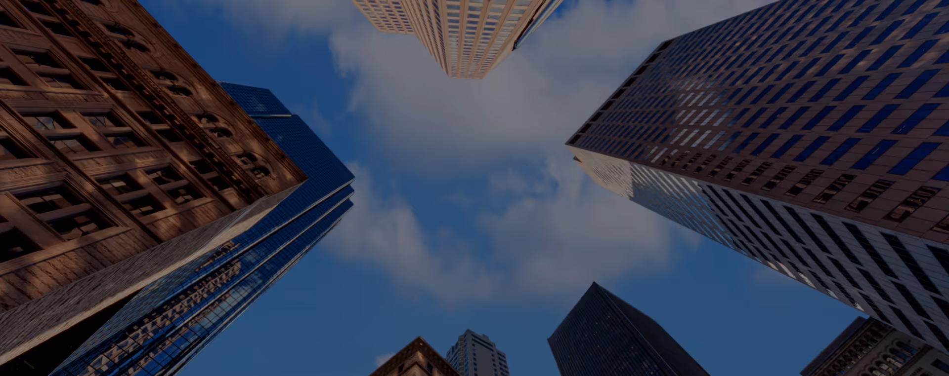Low-angle view of tall skyscrapers against a partly cloudy blue sky in a cityscape.